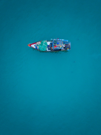 Aerial view of a small fishing boat with green nets floating on the calm blue sea in Vietnam. Aerial view of a small fishing boat with green nets floating on the calm blue sea in Vietnam.