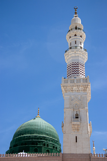 View of the green dome and a tall minaret of Al Masjid e Nabawi against a clear blue sky in Madinah Al Madinah Province Saudi Arabia.