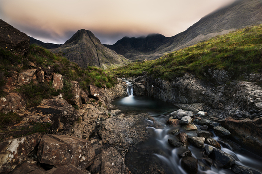 View of the Fairy Pools cascading through a rocky landscape with the Black Cuillin mountains under a dramatic sky Isle of Skye Scotland United Kingdom.