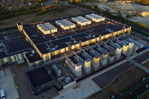 Aerial view of a modern data center facility with numerous HVAC units on the roof surrounding infrastructure and paved areas in the United Kingdom. Aerial view of a modern data center facility with numerous HVAC units on the roof surrounding infrastructure and paved areas in the United Kingdom.