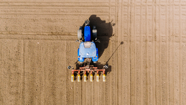 Aerial view of a tractor meticulously planting seeds in neat rows across a vast ploughed field contrasting the machine s blue against the earth s brown Sremska Mitrovica Vojvodina Serbia. Aerial view of a tractor meticulously planting seeds in neat rows across a vast ploughed field contrasting the machine s blue against the earth s brown Sremska Mitrovica Vojvodina Serbia.