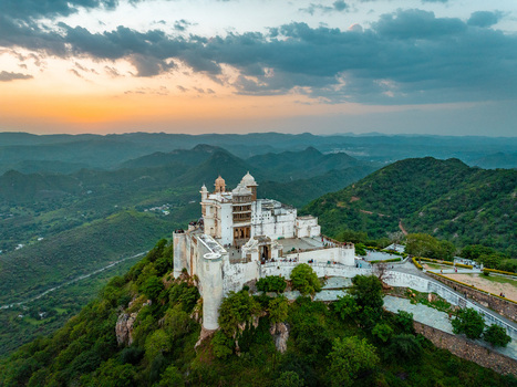 Aerial view of Sajjangarh Palace perched on a hilltop surrounded by the lush green Aravalli hills during a golden sunset in Udaipur Rajasthan India.