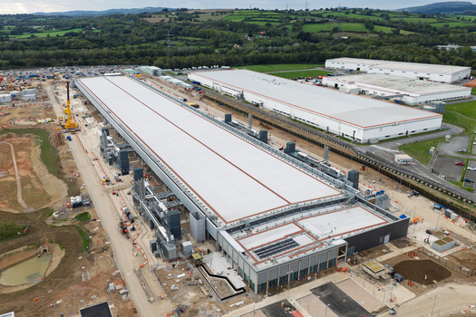 Aerial view of a large data center complex with long flat roofs industrial infrastructure and surrounding green fields in the United Kingdom.