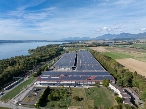 Aerial view of the Decathlon Switzerland logistics center featuring a large solar roof installation situated near Lake Neuchatel surrounded by fields and trees in Onnens Vaud Switzerland. Aerial view of the Decathlon Switzerland logistics center featuring a large solar roof installation situated near Lake Neuchatel surrounded by fields and trees in Onnens Vaud Switzerland.