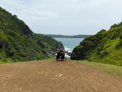 Aerial view of Bukit Pengilon with two people on a bench overlooking the rocky coastline and green hills in Kecamatan Tepus Daerah Istimewa Yogya Indonesia.