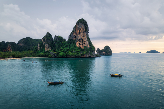 Aerial view of Railay Beach with iconic limestone cliffs rising from the Andaman Sea featuring traditional long tail boats on calm water in Ao Nang Krabi Thailand. Aerial view of Railay Beach with iconic limestone cliffs rising from the Andaman Sea featuring traditional long tail boats on calm water in Ao Nang Krabi Thailand.