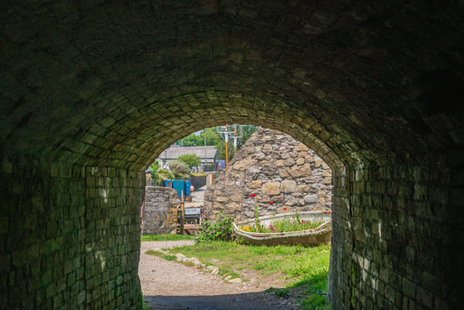 View of a historic brick tunnel framing a garden with a flower filled boat and stone walls in the harbor area of Charlestown Cornwall United Kingdom. View of a historic brick tunnel framing a garden with a flower filled boat and stone walls in the harbor area of Charlestown Cornwall United Kingdom.