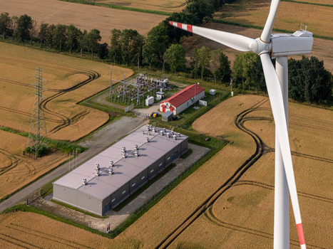Aerial view of a wind turbine and BESS facility next to an electrical substation in a rural field representing sustainable energy infrastructure. Aerial view of a wind turbine and BESS facility next to an electrical substation in a rural field representing sustainable energy infrastructure.
