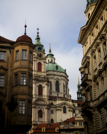 View of St. Nicholas Church with its green domes and clock tower framed by historic buildings under a soft sky in Prague Prague Czechia. View of St. Nicholas Church with its green domes and clock tower framed by historic buildings under a soft sky in Prague Prague Czechia.