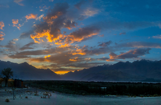 View of the Katpana Desert with sand dunes and silhouetted mountains under a dramatic sunset sky with orange clouds in Skardu Gilgit Pakistan. View of the Katpana Desert with sand dunes and silhouetted mountains under a dramatic sunset sky with orange clouds in Skardu Gilgit Pakistan.