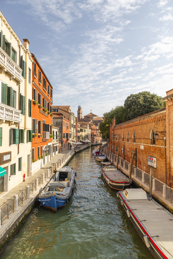View of a narrow canal lined with historic colorful buildings and moored boats under a bright blue sky in Venice Veneto Italy. View of a narrow canal lined with historic colorful buildings and moored boats under a bright blue sky in Venice Veneto Italy.