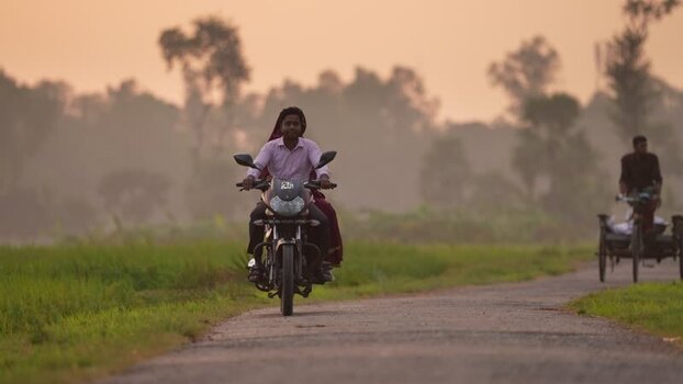 View of a man riding a motorcycle on a rural road Bangladesh.