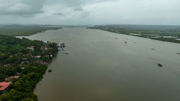 Aerial view of the Mandovi River with lush green banks and small settlements under a cloudy sky Panaji Goa India.