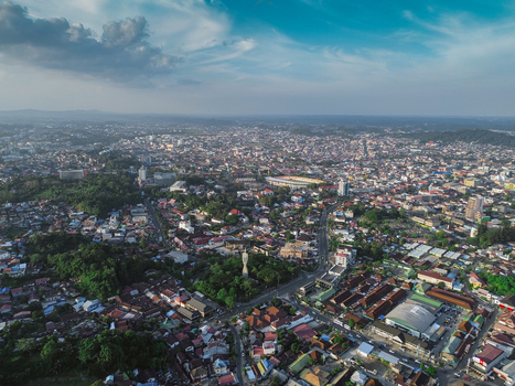 Aerial view of the sprawling urban landscape with dense residential rooftops winding roads and lush green spaces in Samarinda Kalimantan Timur Indonesia. Aerial view of the sprawling urban landscape with dense residential rooftops winding roads and lush green spaces in Samarinda Kalimantan Timur Indonesia.