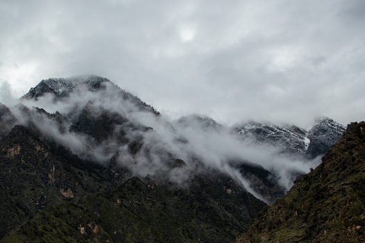 View of rugged mountain peaks partially covered in snow and shrouded in thick white clouds under a moody overcast sky in Chilas Gilgit Pakistan. View of rugged mountain peaks partially covered in snow and shrouded in thick white clouds under a moody overcast sky in Chilas Gilgit Pakistan.