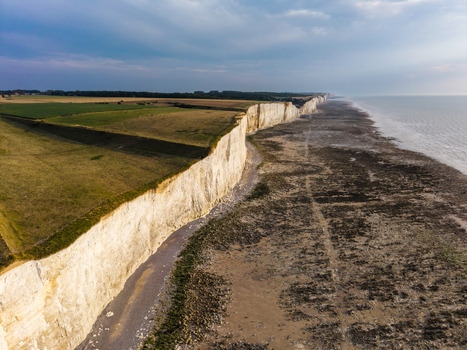 Aerial view of the white chalk cliffs at Beach of the Bois de Cise with green fields above and the vast coastline stretching into the distance in Ault Hauts de France France.