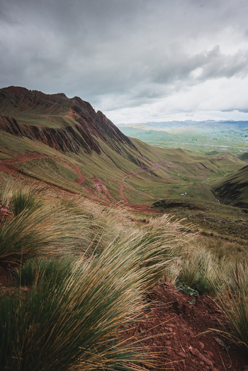View of the rugged landscape and red dirt trails of Pallay Punchu Rainbow Mountain under a dramatic cloudy sky in Layo Cuzco Peru. View of the rugged landscape and red dirt trails of Pallay Punchu Rainbow Mountain under a dramatic cloudy sky in Layo Cuzco Peru.