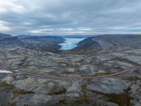 Aerial view of a winding road cuts through the rugged moss covered landscape towards the serene fjord under a vast cloudy sky Westfjords Iceland. Aerial view of a winding road cuts through the rugged moss covered landscape towards the serene fjord under a vast cloudy sky Westfjords Iceland.