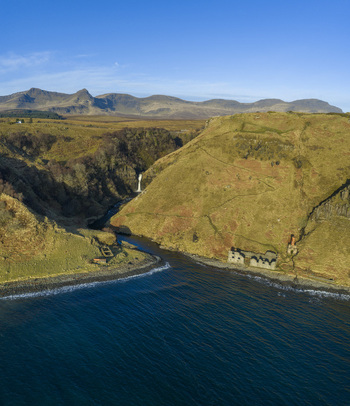 Aerial view of Lealt Falls waterfall cascading through a steep gorge towards the sea with historic ruins on the rocky shore Isle of Skye Scotland United Kingdom. Aerial view of Lealt Falls waterfall cascading through a steep gorge towards the sea with historic ruins on the rocky shore Isle of Skye Scotland United Kingdom.