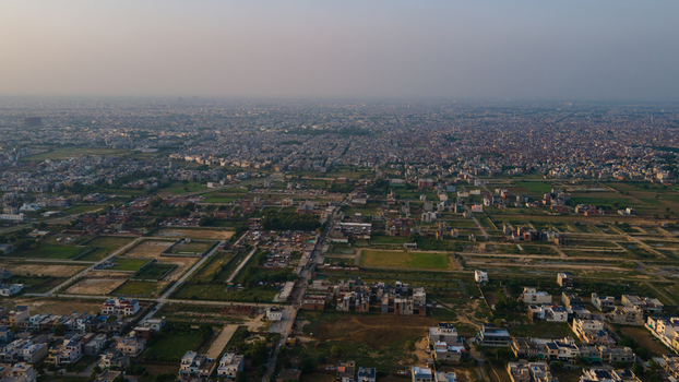 Aerial view of the sprawling urban landscape of Lahore with residential neighborhoods scattered green fields and roads under a hazy sky in Lahore Punjab Pakistan.