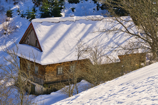 View of a wooden cabin with a snow covered roof nestled on a hillside surrounded by a winter landscape bathed in sunlight Moce Slovakia.