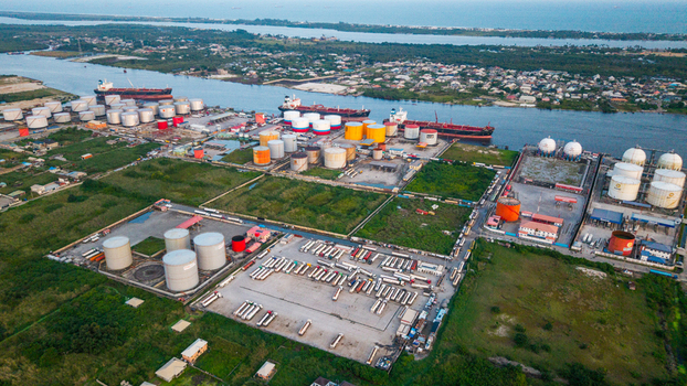 Aerial view of the industrial tank farm and shipping terminal in Satellite Town featuring large storage tanks cargo ships and a parking lot filled with tanker trucks in Lagos Lagos Nigeria.