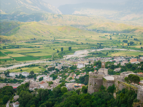 Aerial view of the historic Gjirokaster Fortress with its clock tower overlooking the green valley and river in Gjirokaster Gjirokaster County Albania. Aerial view of the historic Gjirokaster Fortress with its clock tower overlooking the green valley and river in Gjirokaster Gjirokaster County Albania.