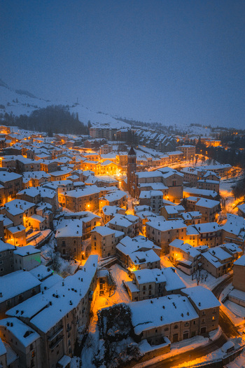 Aerial view of the snow covered town of Rivisondoli at twilight with warm glowing lights illuminating the historic buildings and church tower in Rivisondoli Abruzzo Italy.