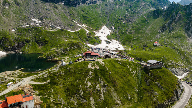 Aerial view of Transfagarasan mountain pass featuring Balea Lake mountain chalets winding roads and snow patches on the green slopes in Curtea de Arges Judetul Arges Romania. Aerial view of Transfagarasan mountain pass featuring Balea Lake mountain chalets winding roads and snow patches on the green slopes in Curtea de Arges Judetul Arges Romania.