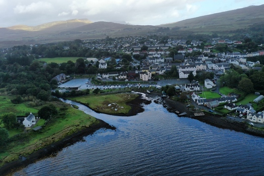 Aerial view of Portree Harbour with its surrounding town buildings lush green hills and coastal inlet in Portree Scotland United Kingdom.