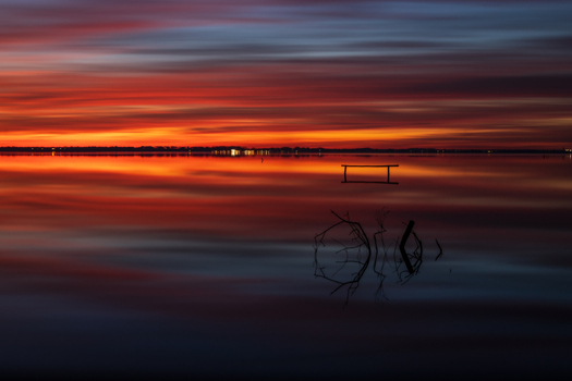 View of Lago di Massaciuccoli with vibrant sunset colors reflecting on the calm water surface and a wooden structure in the foreground Province of Lucca Tuscany Italy.