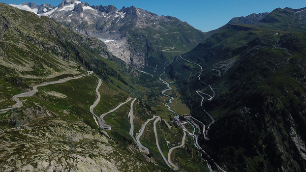 Aerial view of Grimsel Pass featuring winding serpentine roads through rugged mountain peaks and a distant glacier Obergoms Valais Switzerland. Aerial view of Grimsel Pass featuring winding serpentine roads through rugged mountain peaks and a distant glacier Obergoms Valais Switzerland.