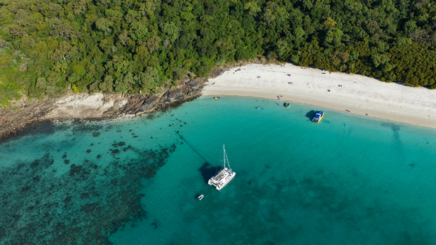 Aerial view of Whitehaven Beach with a catamaran anchored in turquoise water surrounded by lush forest and white sand in Whitsundays Queensland Australia.