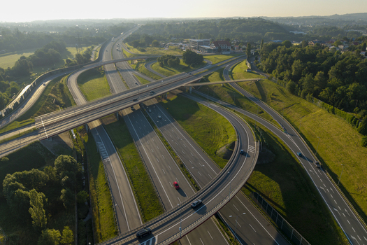 Aerial view of a modern highway interchange with multiple lanes and overpasses surrounded by lush green fields and trees in Poland. Aerial view of a modern highway interchange with multiple lanes and overpasses surrounded by lush green fields and trees in Poland.