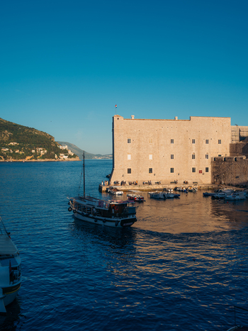 View of St. John s Fortress and the historic old harbor with boats moored on the calm blue water under a clear sky in Dubrovnik Dubrovnik Neretva County Croatia. View of St. John s Fortress and the historic old harbor with boats moored on the calm blue water under a clear sky in Dubrovnik Dubrovnik Neretva County Croatia.