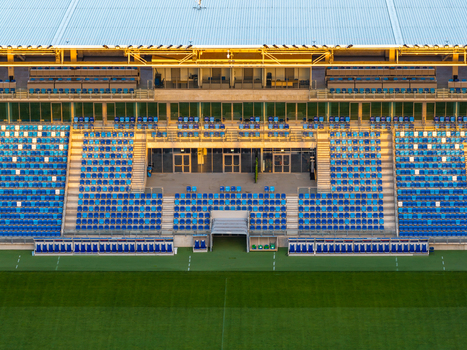 Aerial view of the football stadium featuring rows of blue seats a green pitch and warm golden hour light illuminating the grandstand in Plock Mazowieckie Poland.