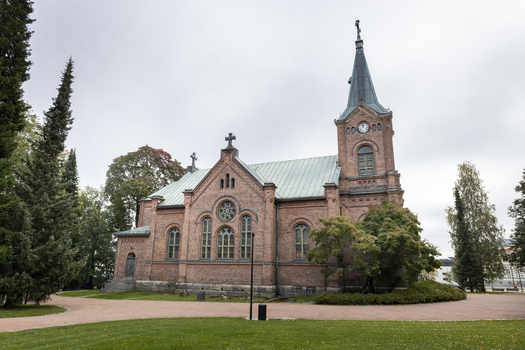 View of the historic red brick Jyvaskyla City Church with its tall steeple arched windows and green metal roof set amidst trees and a gravel path in Jyvaskyla Central Finland Finland.