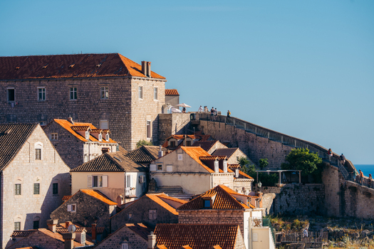 View of the historic stone buildings and terracotta rooftops of Dubrovnik Old Town with people walking along the ancient city walls under a clear blue sky in Dubrovnik Dubrovnik Neretva County Croatia. View of the historic stone buildings and terracotta rooftops of Dubrovnik Old Town with people walking along the ancient city walls under a clear blue sky in Dubrovnik Dubrovnik Neretva County Croatia.