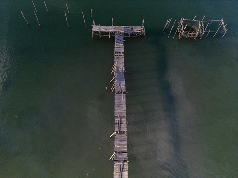 Aerial view of the weathered wooden pier at Galang Baru stretching over calm turquoise waters with wooden poles and fishing structures Galang Riau Islands Indonesia. Aerial view of the weathered wooden pier at Galang Baru stretching over calm turquoise waters with wooden poles and fishing structures Galang Riau Islands Indonesia.