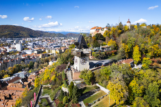 Aerial view of the iconic clock tower the Grazer Uhrturm watches over the autumn painted city from Schlossberg hill Graz Styria Austria.