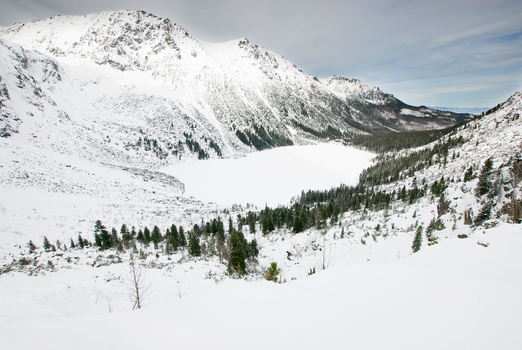 View of the frozen Morskie Oko lake surrounded by snow covered Tatra Mountains and evergreen trees under a cloudy sky Tatra County Lesser Poland Voivode Poland. View of the frozen Morskie Oko lake surrounded by snow covered Tatra Mountains and evergreen trees under a cloudy sky Tatra County Lesser Poland Voivode Poland.