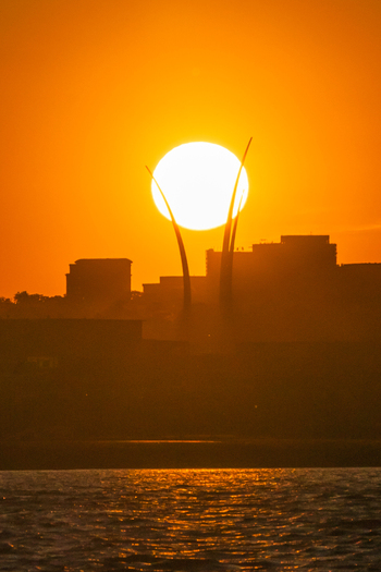 View of the Air Force Memorial spires silhouetted against a large setting sun over the city skyline and water in Washington District of Columbia United States. View of the Air Force Memorial spires silhouetted against a large setting sun over the city skyline and water in Washington District of Columbia United States.