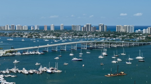 Aerial view of Peanut Island and the Blue Heron Bridge with numerous boats anchored in the turquoise water of Lake Worth Lagoon Palm Beach County Florida United States.