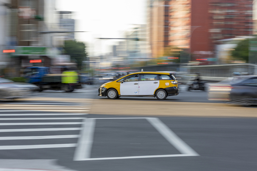 View of a yellow and white taxi cab driving through a busy urban intersection with motion blur and city buildings in the background Taipei City Taiwan. View of a yellow and white taxi cab driving through a busy urban intersection with motion blur and city buildings in the background Taipei City Taiwan.