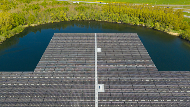 Aerial view of a large floating solar farm with rows of photovoltaic panels on a calm lake surrounded by lush green trees in Zwolle Overijssel Netherlands. Aerial view of a large floating solar farm with rows of photovoltaic panels on a calm lake surrounded by lush green trees in Zwolle Overijssel Netherlands.