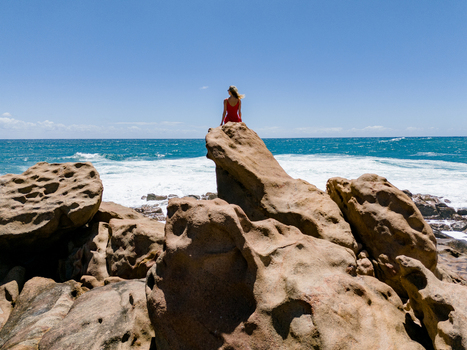 Aerial view of a woman in a red dress sitting on a large rock formation overlooking the turquoise ocean waves at Injidup Natural Spa Yallingup Western Australia Australia. Aerial view of a woman in a red dress sitting on a large rock formation overlooking the turquoise ocean waves at Injidup Natural Spa Yallingup Western Australia Australia.