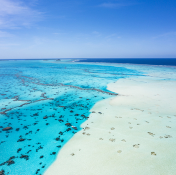 Aerial view of the turquoise Aitutaki lagoon with shallow sandbanks coral reefs and deep blue ocean under a clear sky in Aitutaki Cook Islands. Aerial view of the turquoise Aitutaki lagoon with shallow sandbanks coral reefs and deep blue ocean under a clear sky in Aitutaki Cook Islands.