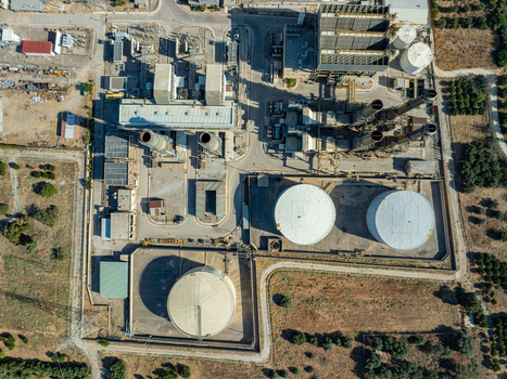 Aerial view of a large industrial power plant facility with storage tanks chimneys and infrastructure surrounded by rural landscape in Chania Greece.