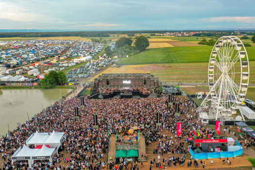 Herzogenaurach Germany 24 July 2025 Aerial view of the Open Beatz Festival featuring a massive crowd in front of a large stage and a ferris wheel under a cloudy sky.