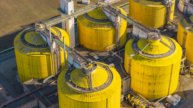 Aerial view of large yellow anaerobic digestion tanks and industrial pipelines at a wastewater treatment and biogas facility in Italy.